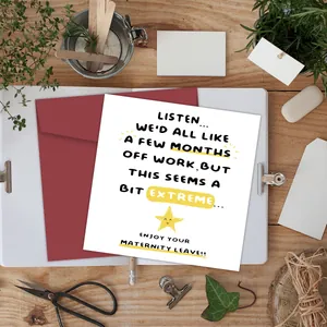 Funny maternity leave card with a red envelope on a rustic wooden desk with stationery