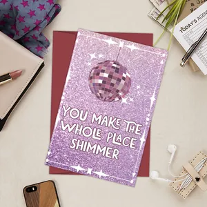 Detail of shimmer disco ball birthday card with red envelope on a cozy desk setup