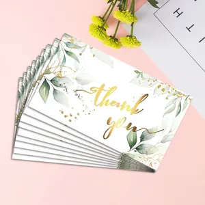 Close-up of white floral thank you cards with gold foil text and green leaves