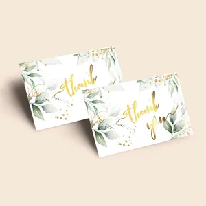 Close-up of elegant thank you cards with gold lettering and green watercolor leaf designs