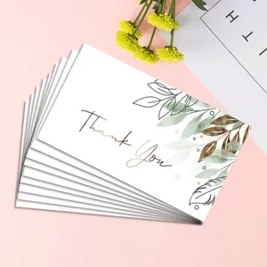 Close-up of stacked thank you cards with gold foil text and green leaf illustrations