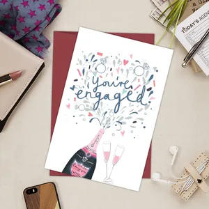 Detailed view of hand-drawn engagement card with burgundy envelope and lifestyle items