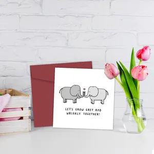 Square greeting card with cartoon elephants and red envelope on a white desk
