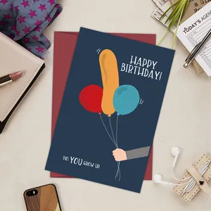 Funny birthday card with a naughty balloon illustration and a red envelope on a desk