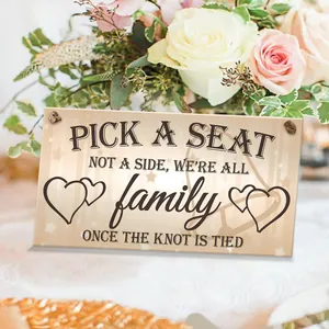 Detail of wooden wedding sign with 'Pick a Seat Not a Side' text among pink roses