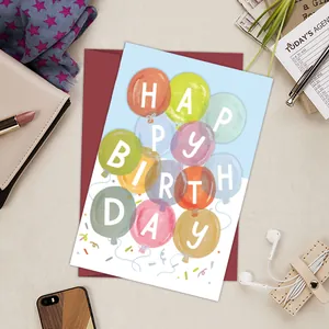 Funny birthday card with colorful balloons and a red envelope on a beige desk flatlay