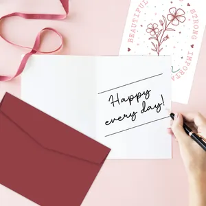 Close-up of a hand writing on a greeting card set with a deep red envelope and floral card