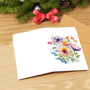 Biglietto d'auguri piegato con fiori ad acquerello e busta in carta kraft su legno