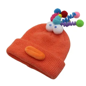 Detail of funny orange knitted beanie with googly eyes and colorful pom-pom spirals
