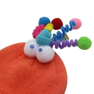 Detail of orange knitted hat featuring cartoon eyes and colorful spiral tentacles with pom-poms