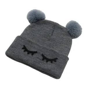 Detail van grijze gebreide babymuts met zachte bontpompons en geborduurde wimperpatroon