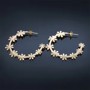 Elegant gold flower hoop earrings with daisy design over a dark blue mirror surface
