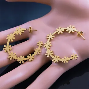 Close-up of golden floral hoop earrings on a hand model showcasing realistic size scale