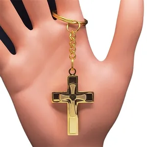 Golden stainless steel cross keychain with black geometric patterns held by hand