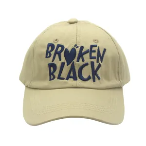 Macro shot of khaki baseball cap with navy 'BROKEN BLACK' heart embroidery detail