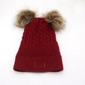 Detail of burgundy knit hat featuring two large brown pom-poms and ribbed cuff