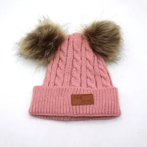Detail of pink cable knit kids beanie with double brown faux fur pom-poms and leather tag