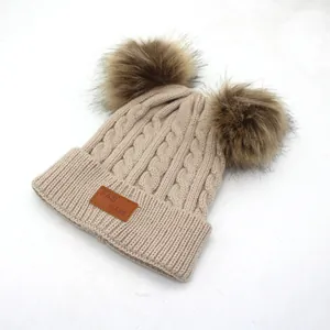 Detailed knit texture of beige double pompom hat with brown leather brand label