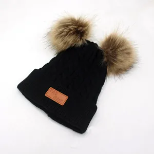 Detail of black knit beanie with double faux fur pom-poms and leather logo patch