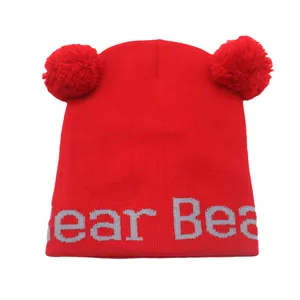 Dettaglio del berretto in maglia rossa con doppio pompon e scritta bear ricamata