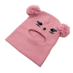 Dettaglio passamontagna rosa in maglia con ricamo a gatto e morbidi pompon doppi