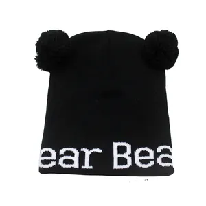 Dettaglio cappello in maglia nero per bambini con due pompon e scritte bianche ricamate