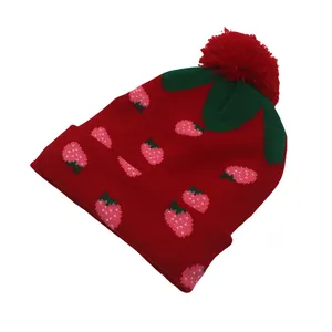 Detail van rode aardbei gebreide muts met groene bladeren en een pluizige rode pompon