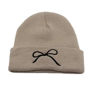 Close-up of beige knit beanie featuring detailed black bow embroidery on the folded brim
