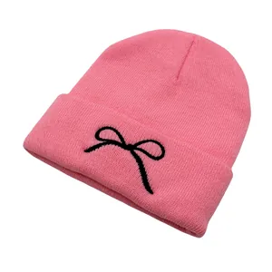 Close-up of pink ribbed knit beanie featuring a black embroidered bow detail on the cuff