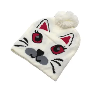 Détail du motif jacquard chat et pompon moelleux sur bonnet en tricot blanc crème