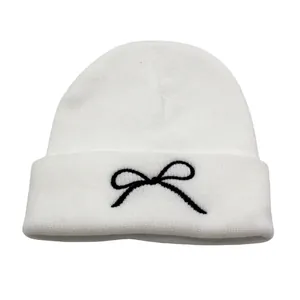 Close-up of black bow embroidery detail on soft white ribbed knit winter beanie hat