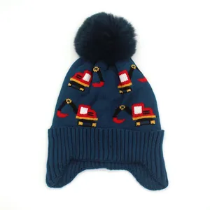 Close-up of knit texture and fluffy pom-pom on navy blue excavator pattern winter hat