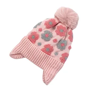 Détail du bonnet en tricot rose avec fleurs 3D et pompon en fausse fourrure douce