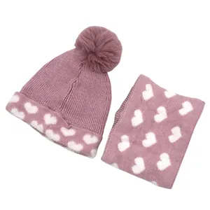 Pink knit hat and scarf set with white heart patterns and a fluffy faux fur pompom