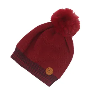 Details der burgunderroten Winterstrickmütze mit einem flauschigen Kunstpelz-Bommel-Dekor