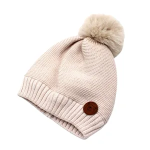 Detailansicht der cremefarbenen Strickmütze mit Pompon und Lederpatch mit Bär