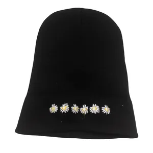 Dettaglio di sei ricami di margherite bianche sul berretto di maglia nera invernale