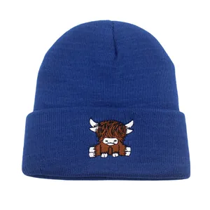 Close-up of a navy blue knit beanie featuring detailed Highland Cow embroidery on the cuff