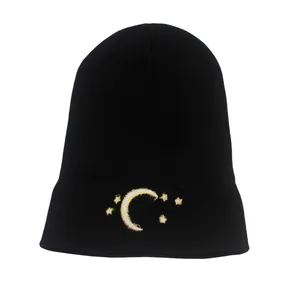 Detailed close-up of yellow moon and white star embroidery on a black knit beanie