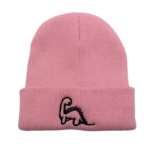 Détail d'un bonnet en tricot rose avec un petit dinosaure noir brodé sur le rebord replié
