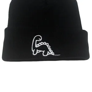 Gros plan d'un bonnet noir en tricot avec une broderie de dinosaure blanc sur le bord plié