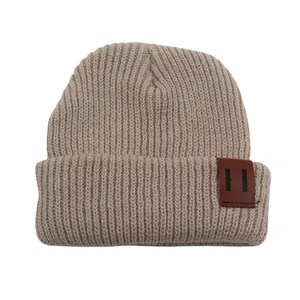 Close-up of the ribbed knit texture and brown leather patch on a beige beanie hat