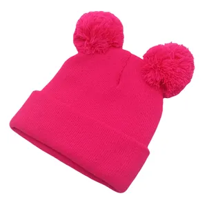 Dettaglio del cappello in maglia rosa fucsia con due grandi pompon e bordo con risvolto