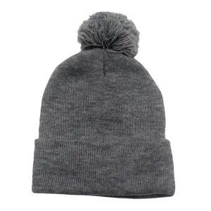 Berretto in maglia grigio scuro con pompon e risvolto su uno sfondo bianco pulito