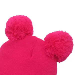 Dettaglio di un berretto in maglia rosa acceso con due grandi pompon soffici coordinati in cima