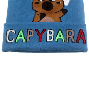 Dettaglio del berretto in maglia blu con un capibara e testo jacquard pixelato
