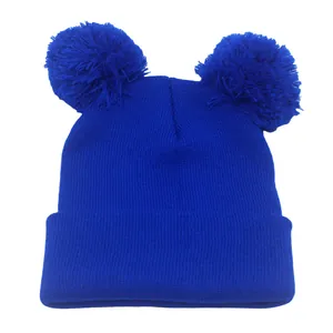 Dettaglio del berretto in maglia blu con due pompon di pelliccia e bordo a costine