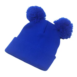 Dettaglio di un berretto in maglia blu reale con due grandi pompon coordinati