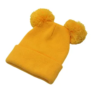 Dettaglio del berretto in maglia giallo con doppi pompon in pelliccia e risvolto