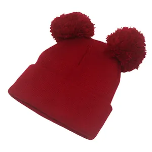 Dettaglio del berretto rosso in maglia con doppi pompon e trama invernale a coste